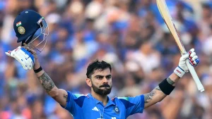 Virat Kohli raises his bat and helmet in celebration after scoring a century for India during an international cricket match.