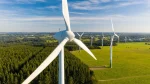 Aerial view of wind turbines generating renewable energy over green farmland and forest landscape on a clear day