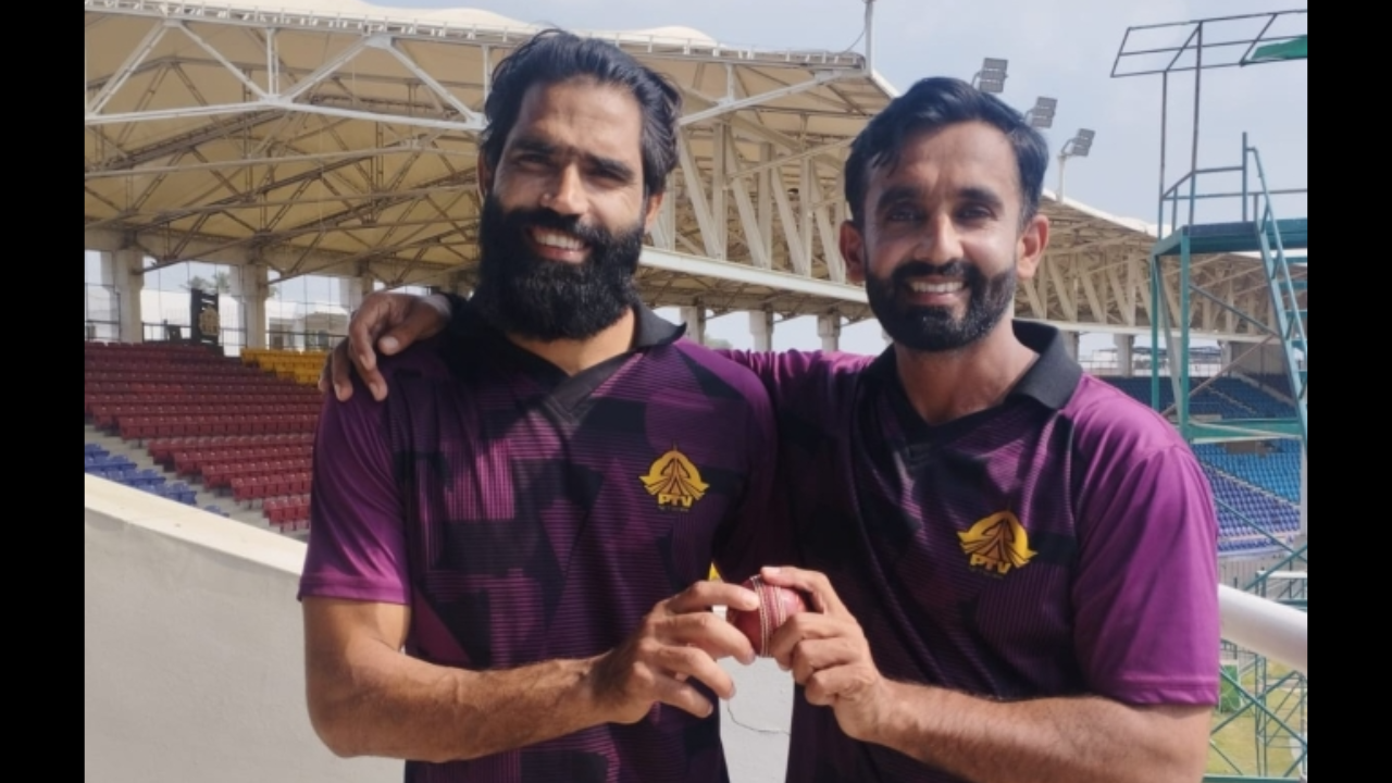 Ali Usman and Amad Butt of PTV cricket team smiling and holding a red cricket ball together at a stadium in 2026.