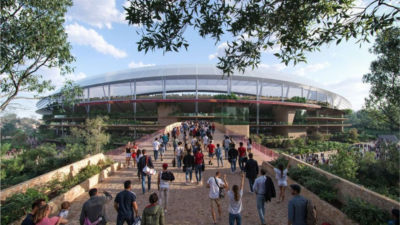 Large crowd walking towards a modern, eco-friendly stadium surrounded by lush greenery and trees on a sunny day