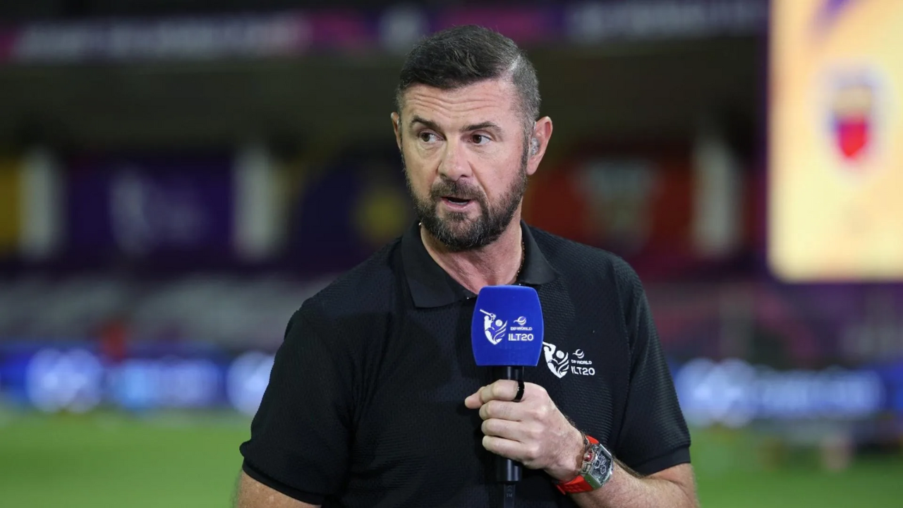 Cricket commentator speaking during a live DP World ILT20 broadcast, holding a branded microphone on the field