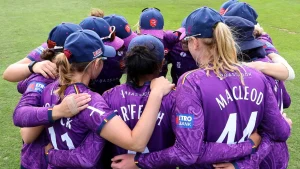 Essex Women's cricket team players wearing purple jerseys in a pre-match huddle on the field.
