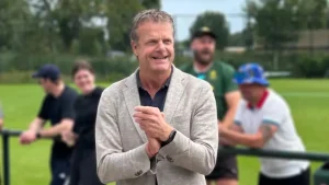 Guido Landheer, chairman of the KNCB, smiling and clapping at a cricket event with people in the background on a grassy field.
