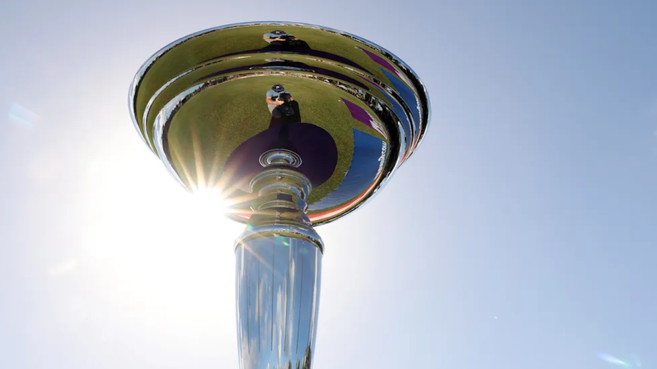 The ICC U19 Cricket World Cup trophy shines in the sunlight with a clear blue sky in the background.