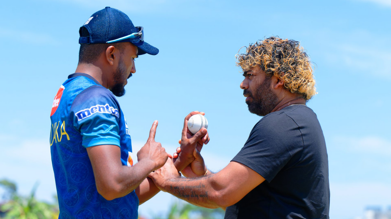 Legendary Sri Lankan pacer Lasith Malinga coaches a young Sri Lanka bowler on grip and technique during a training session under clear skies.
