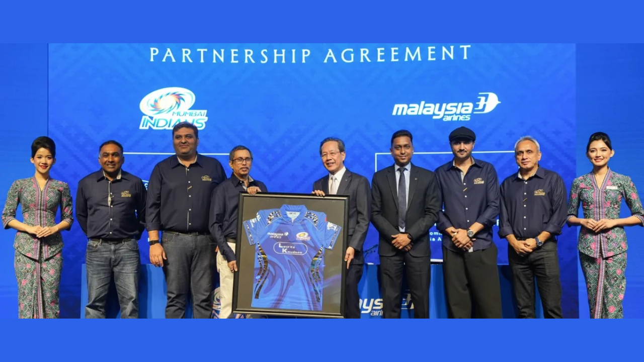 Mumbai Indians and Malaysia Airlines representatives during official partnership announcement, holding framed team jersey at media event.