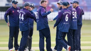 Scotland men's cricket team players in navy and purple kits celebrating on the field during a match, with visible names including Berrington, Watt, Sharif, and O Davidson.