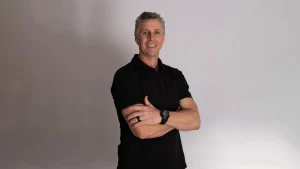 Troy Cooley poses in a black shirt for a professional profile photo against a plain background