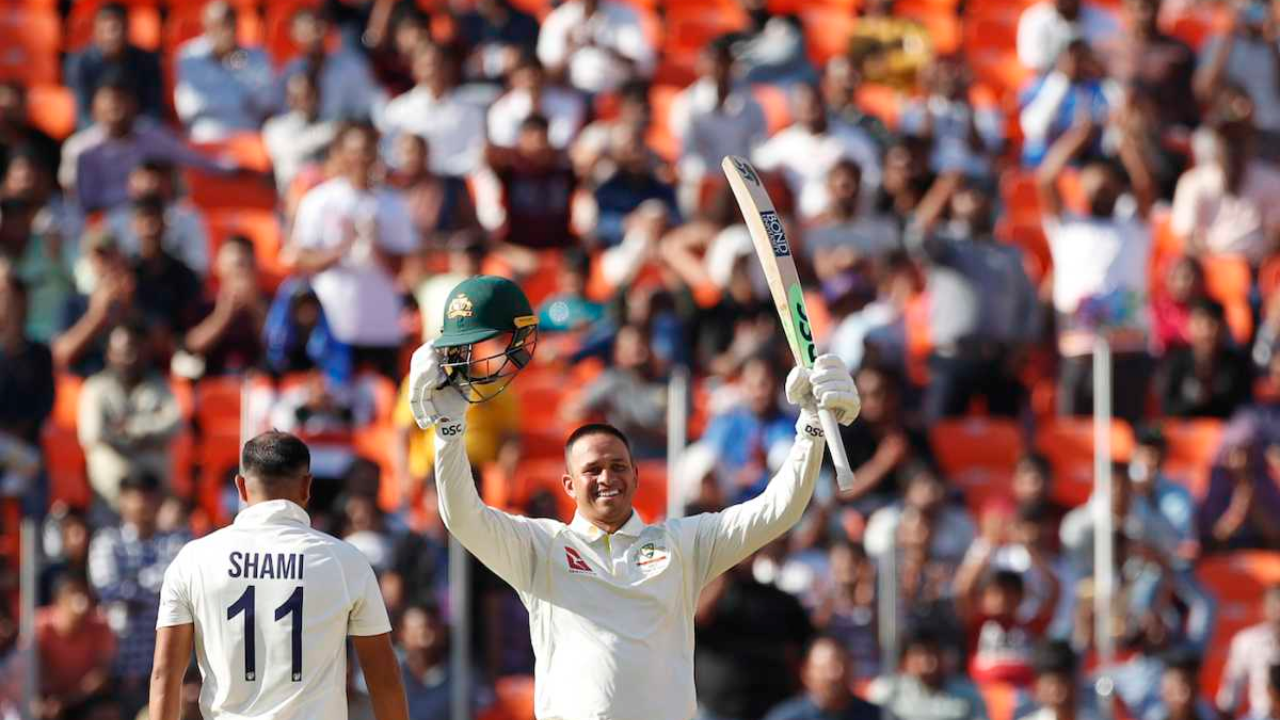 Usman Khawaja celebrates a century during a test match against India, raising his bat and helmet as Mohammed Shami walks past