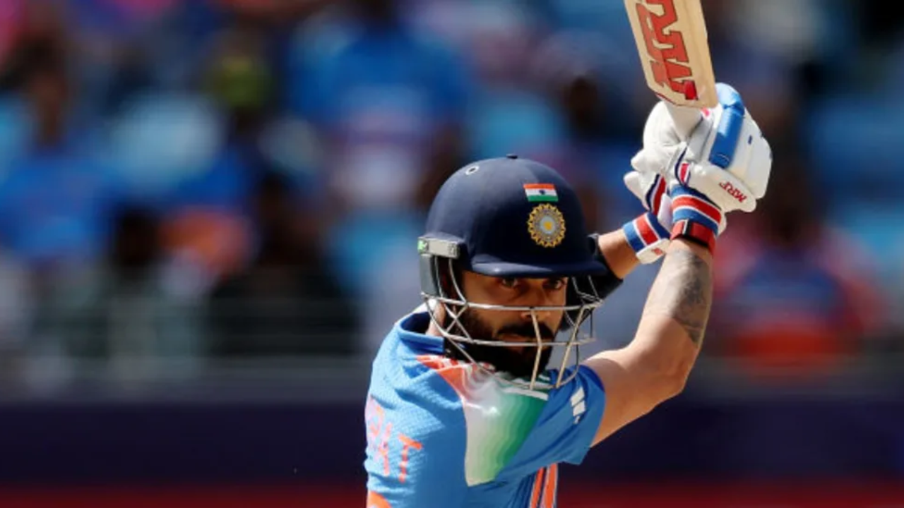 Virat Kohli in Indian cricket team jersey playing a shot during a match, focused and mid-swing with bat raised.
