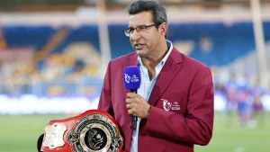 Wasim Akram presenting during ILT20 cricket coverage while holding a championship-style belt on the field