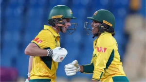 Beth Mooney and Alana King celebrate between wickets during an Australia women’s cricket match, wearing yellow uniforms and green helmets.