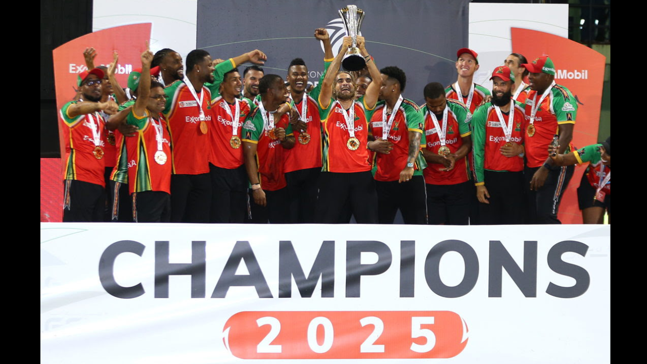 Guyana Amazon Warriors players celebrate after winning the 2025 cricket championship, lifting the trophy on stage with medals around their necks.