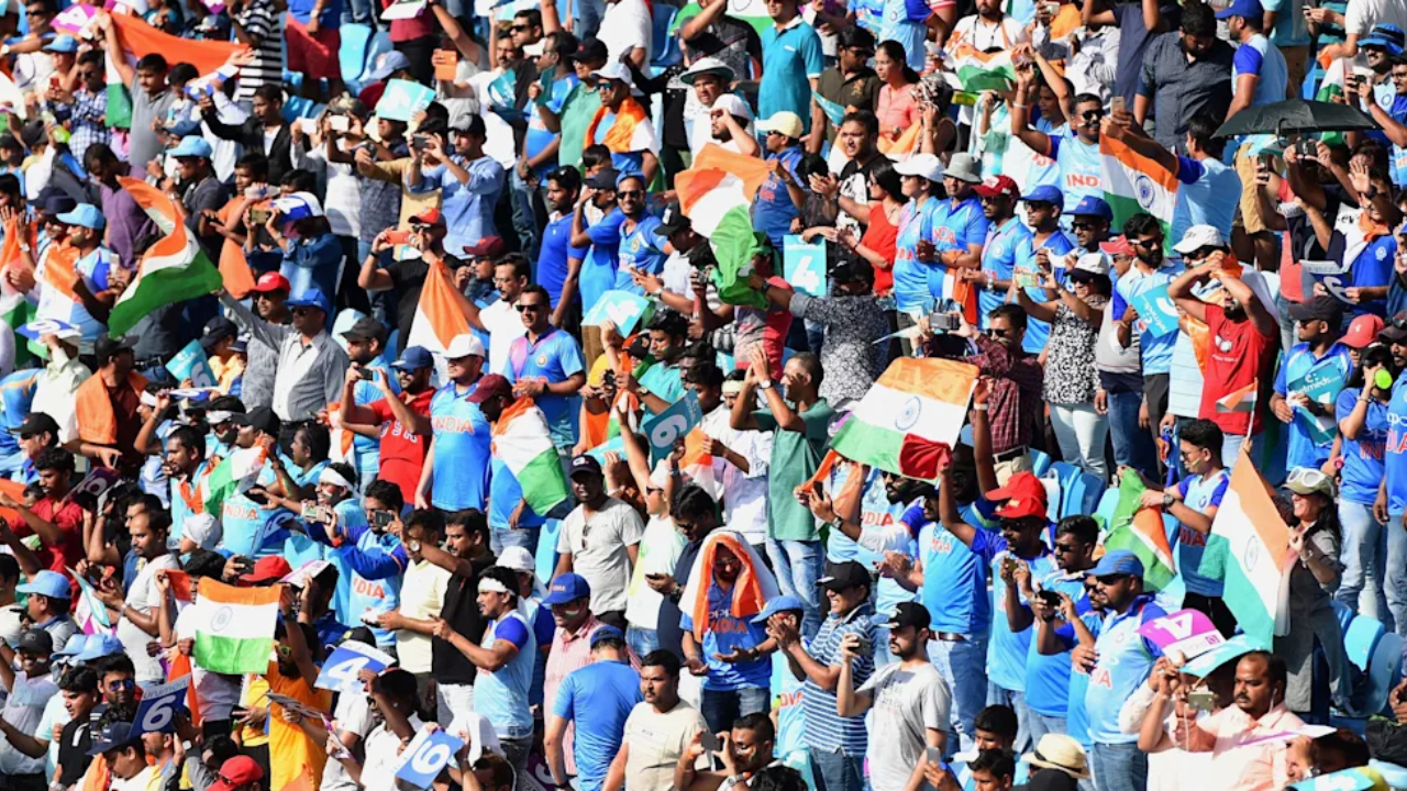 Indian cricket fans in blue jerseys waving national flags and cheering in a packed stadium during a match