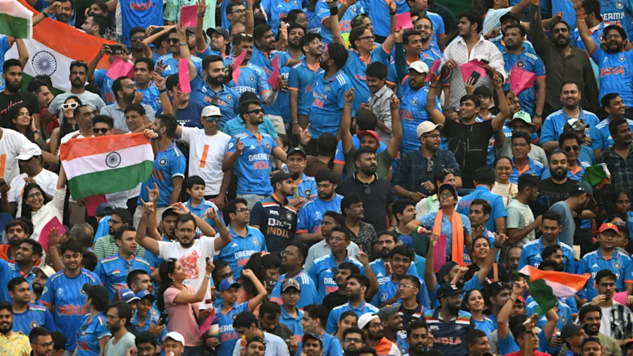 Indian cricket fans wearing blue jerseys and waving national flags while cheering in a packed stadium