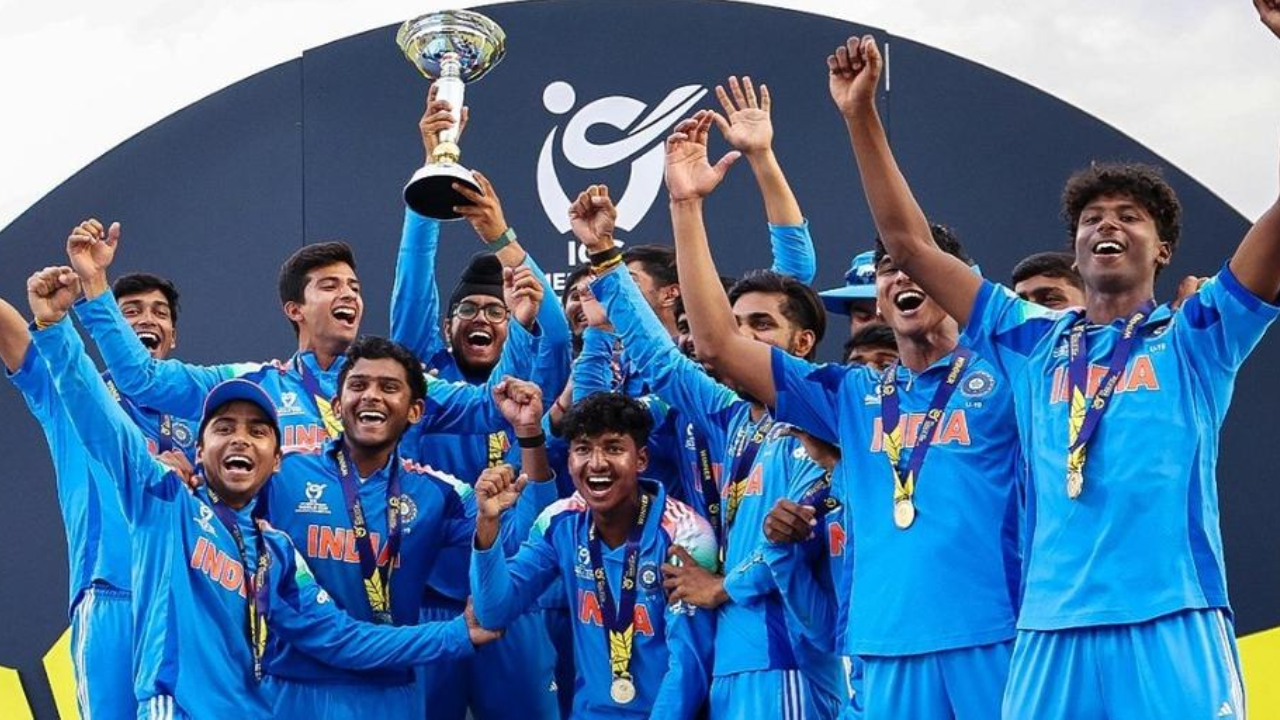 India U19 cricket team celebrates winning the ICC U19 World Cup 2026, players cheer with the trophy on the podium.