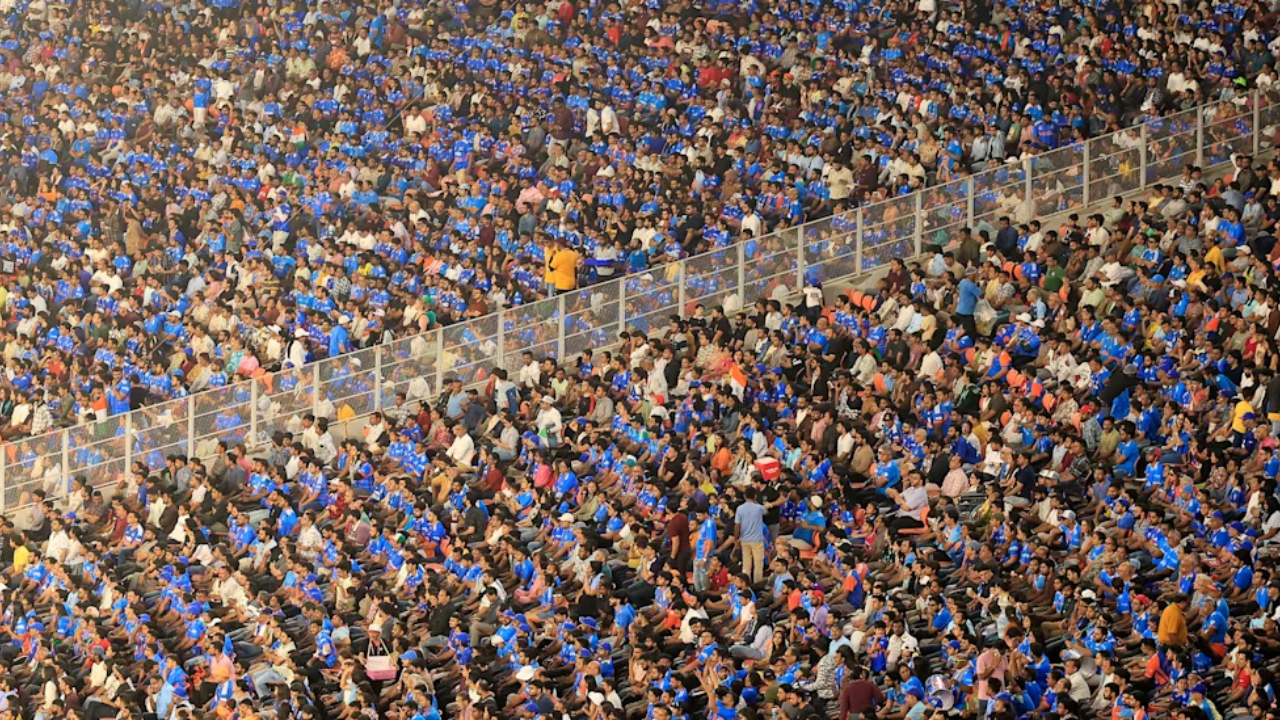 Packed IPL stadium with thousands of fans wearing blue jerseys during a high-energy cricket match in India.