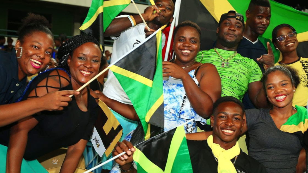 Group of Jamaican cricket fans smiling and waving national flags in the stadium stands during an international match.