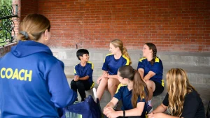 Women and girls participating in a Metro Bank cricket coaching session with a coach addressing the team on outdoor steps