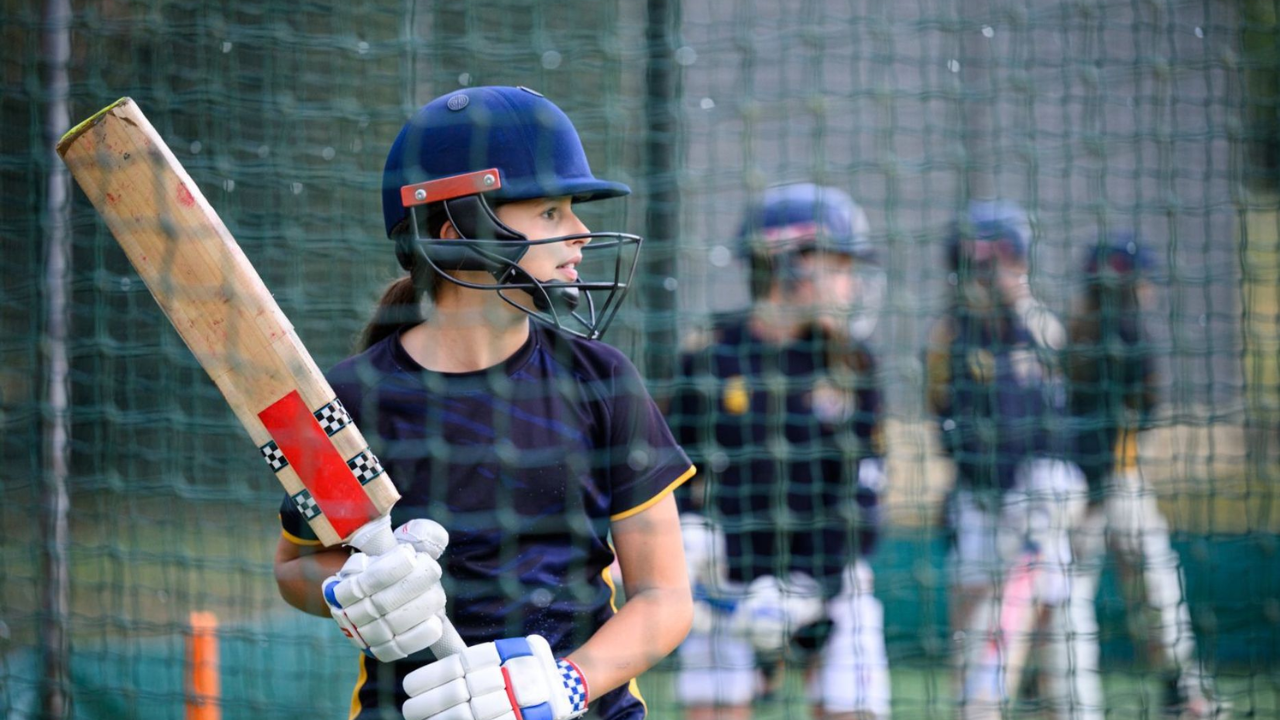 Young female cricketer batting in practice nets wearing helmet and gloves, representing the Metro Bank Women’s and Girls Cricket Collection 2025.