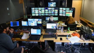 Broadcast control room with multiple monitors and technicians managing live sports production feed