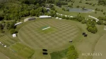 Aerial view of the Wormsley cricket ground in England surrounded by lush greenery, practice nets, and white marquees