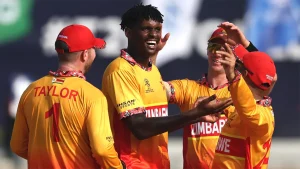 Zimbabwe national cricket team players celebrating a wicket during an international match, wearing yellow and red kits.
