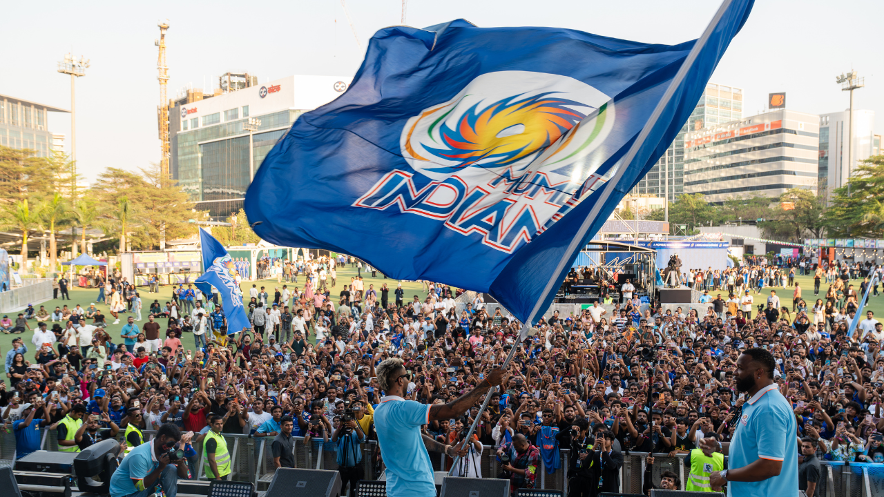 Hardik Pandya waving Mumbai Indians flag at The Mix fan event with large crowd of supporters in background