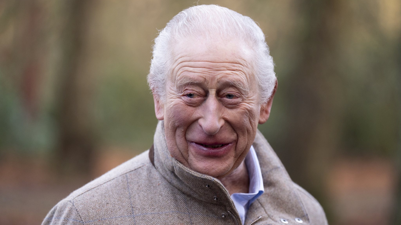 Portrait of King Charles III, the British monarch, smiling outdoors while wearing a beige coat.