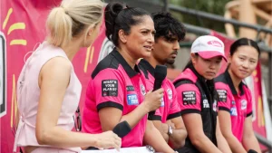 Lisa Sthalekar speaking into a microphone while wearing a Sydney Sixers jersey during a Women’s Big Bash League team event.