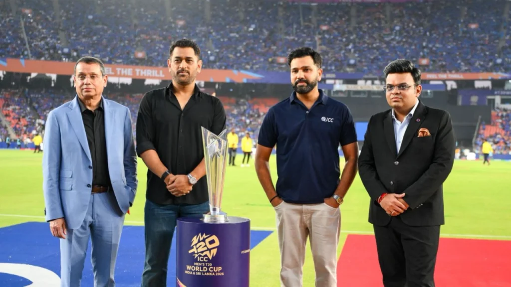 MS Dhoni, Rohit Sharma, and ICC chairman Jay Shah standing with the ICC Men’s T20 World Cup 2026 trophy at a stadium event.