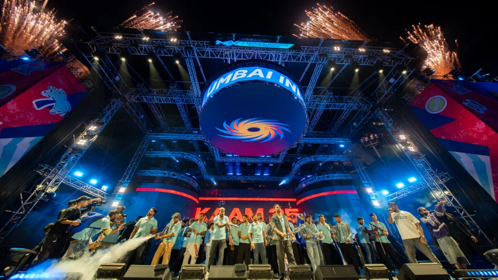 Mumbai Indians team on stage at The MIX event with fireworks, lights and players celebrating in front of crowd