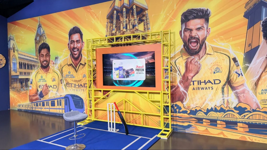 Chennai Super Kings IPL fan zone display with large player artwork including MS Dhoni and Virat Kohli and cricket setup indoors