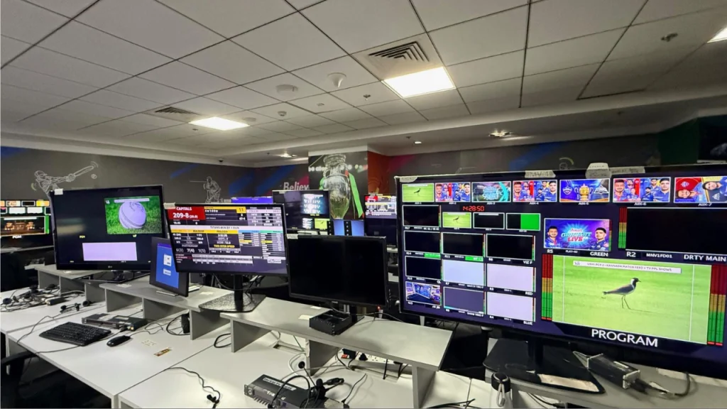 Cricket broadcast control room with multiple monitors displaying live match production feeds and graphics systems