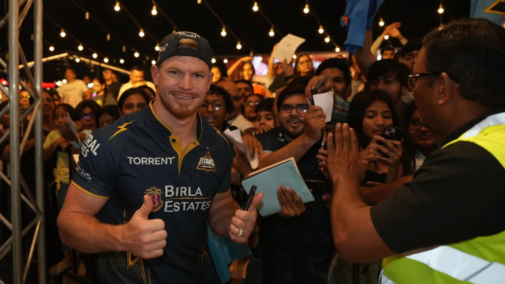 Glenn Phillips of Gujarat Titans interacting with fans, giving autographs and posing with thumbs up during a crowded night event with string lights in the background