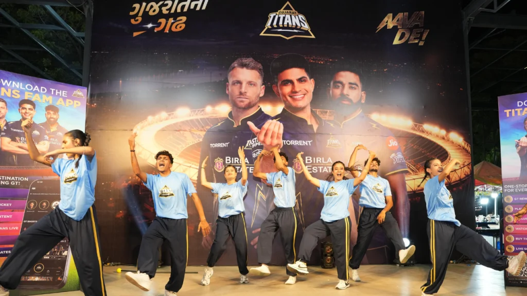 Dance group performing on stage at Gujarat Titans fan event with large team poster backdrop and crowd entertainment at Frizbee Food Park
