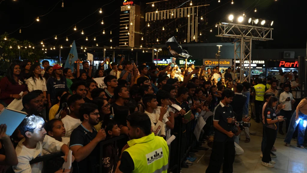 Large crowd of Gujarat Titans fans gathered at Frizbee Food Park cheering and holding banners during a live team event at night with decorative lights