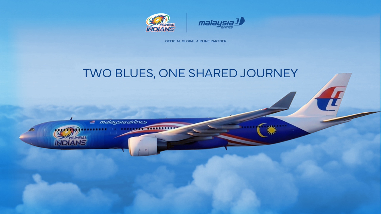 Mumbai Indians branded Malaysia Airlines aircraft flying above clouds with partnership slogan “Two Blues, One Shared Journey” displayed.