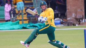 Rassie van der Dussen playing a cricket shot in South Africa jersey during a match, wearing batting gear and helmet on the field