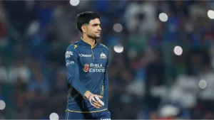 Shubman Gill in Gujarat Titans jersey during an IPL match, walking on the field with blurred stadium crowd in the background.