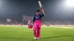 Vaibhav Sooryavanshi raises his bat in celebration during an IPL match wearing Rajasthan Royals jersey in a packed stadium at night