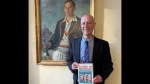 Author Richard Whitehead holding his book “Victory in Australia,” winner of the Cricket Society and MCC Book of the Year Award, standing beside a historic cricket portrait.