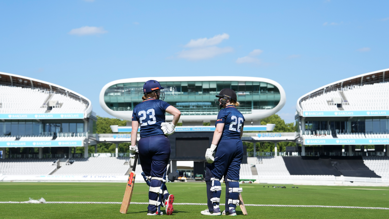Two women cricketers walking onto the pitch at Lord’s Cricket Ground in London with bats and full gear during a match or practice