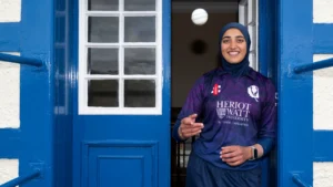 Abtaha Maqsood, Scotland women’s cricketer, standing in a doorway wearing a Heriot-Watt University cricket jersey.