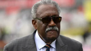 Former West Indies cricket captain Clive Lloyd wearing sunglasses and a suit at a cricket venue.