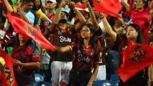Cricket fans waving red flags and cheering in a packed stadium during a CPL match