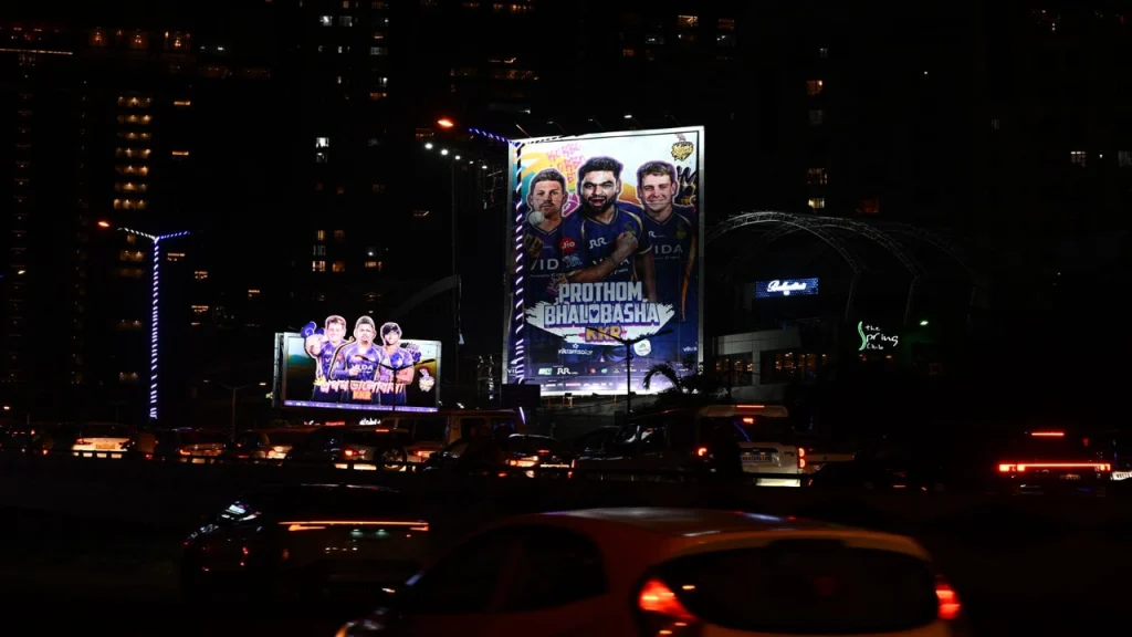Kolkata Knight Riders IPL billboards lighting up a busy Kolkata street at night featuring players and Prothom Bhalobasha campaign branding