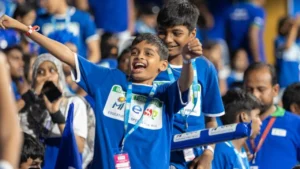Young Mumbai Indians fans celebrating in the stands during MI’s #ESAMatchDay 2026 event while wearing blue campaign shirts and cheering at the stadium.