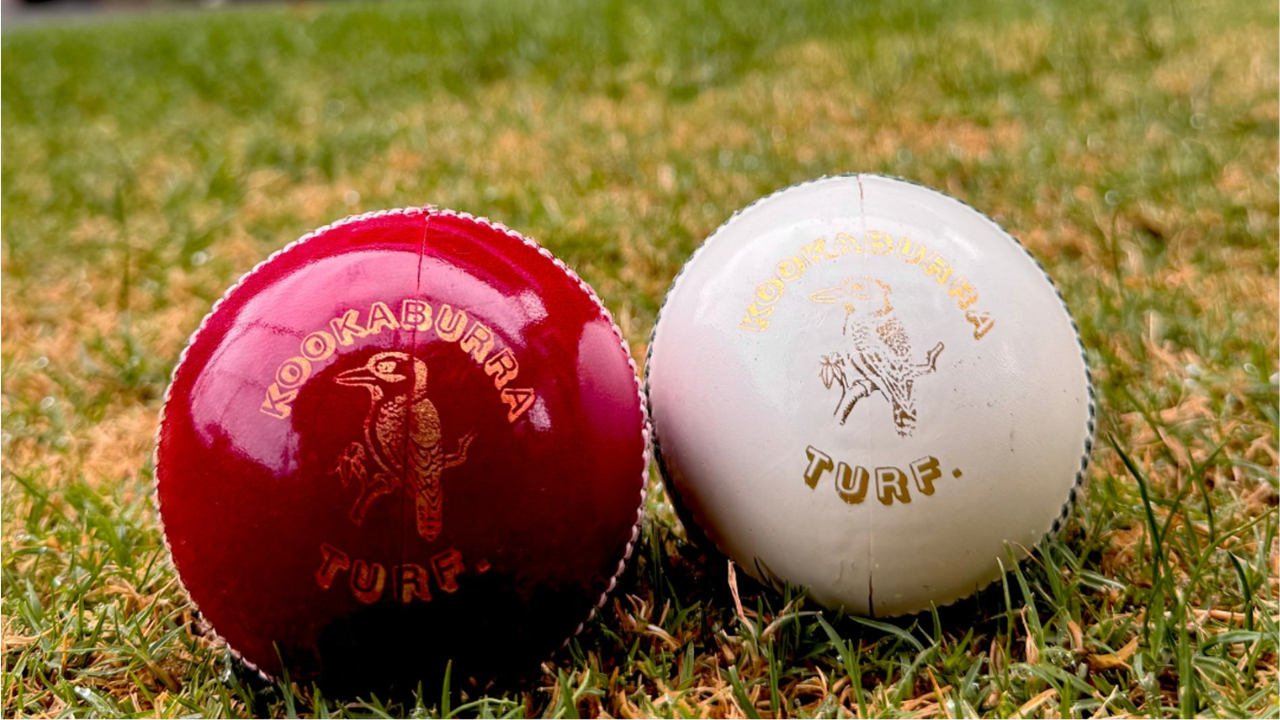 Red and white Kookaburra Turf cricket balls placed on grass field, commonly used in professional cricket matches and training sessions.