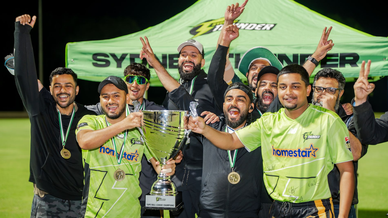 Tape ball cricket champions celebrating with a trophy and medals in front of a Sydney Thunder tent after winning a tournament.